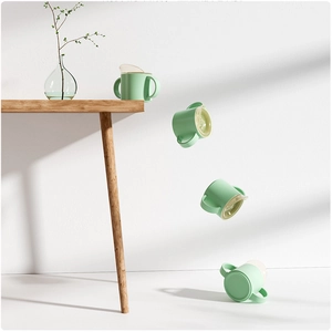 Green baby sippy cup with dual handles shown falling to demonstrate drop resistance