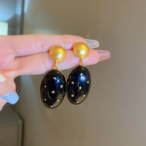 Detail of vintage gold and black oval earrings featuring gold star patterns on enamel