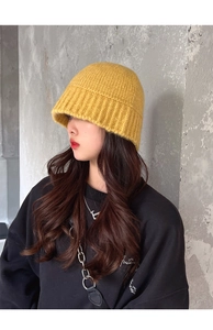 Detail showing bright yellow chunky knit bucket hat on model against industrial grey wall
