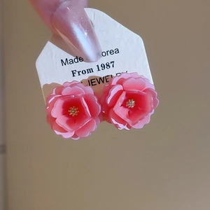 Détail de boucles d'oreilles fleurs en résine rose avec étamines dorées sur présentoir