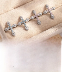 Macro detail of cross cartilage earrings with blue and pink zircons on velvet