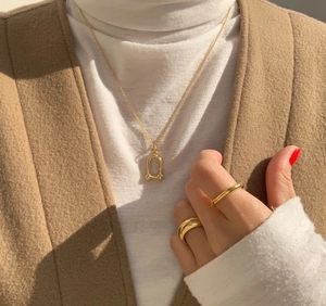 Detail of horseshoe pendant necklace and gold rings styled on model with knitwear