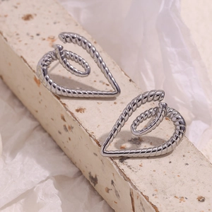 Macro detail of silver twist rope heart earrings on a textured stone surface