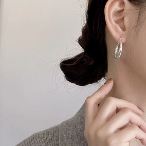 Macro detail of silver twisted hoop earrings worn by a model in a minimalist setting