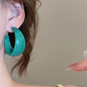 Détail d'une boucle d'oreille en résine verte en forme de C portée par un mannequin