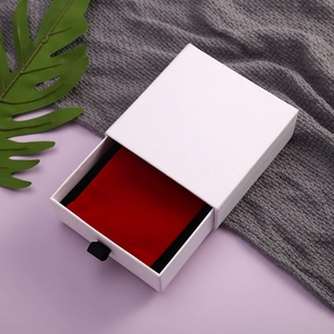 Close-up of white drawer jewelry box with red velvet pouch and green leaf accent