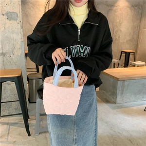 Detailed close-up of quilted pink puffer handbag with blue handles held by a model