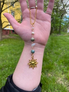 Detail of a gold beaded sun pendant chain with colorful crystals held in an outdoor setting