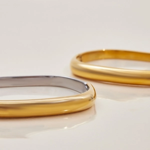 Dettaglio di bracciali rigidi quadrati lucidi in oro e argento con chiusura a scatto
