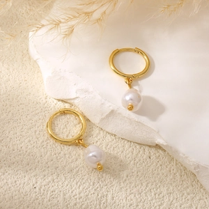 Detail of gold hoop earrings with baroque pearl drops on a white stone display stand