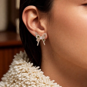 Close-up of golden butterfly earring with white and green stones on model ear