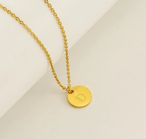 Gros plan du pendentif circulaire doré avec la lettre D gravée sur collier en acier