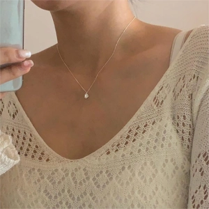 Detailed view of a gold collarbone necklace featuring a white teardrop pendant on a model
