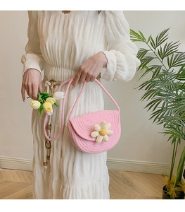 Detail of pink woven saddle bag featuring a white daisy flower and a braided shoulder strap