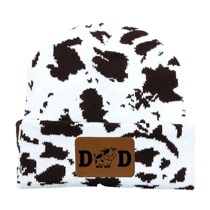 Detail of a cow print knit beanie featuring a brown leather patch with DAD text