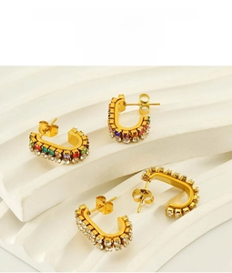 Close-up of gold-plated stud earrings with colorful rhinestones on a white plaster base