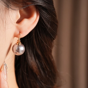 Close-up of a model wearing vintage gold hoop earrings with a large grey pearl drop