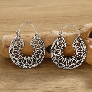 Detailed view of silver bohemian drop earrings with intricate hollow patterns on driftwood