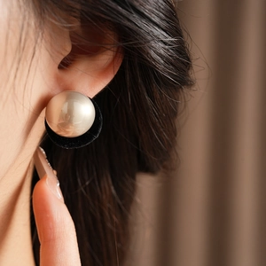 Macro view of a classic round pearl earring with black velvet base on ear