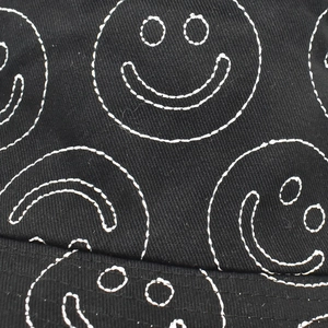 Close-up of white smiling face embroidery on black canvas fabric of a bucket hat