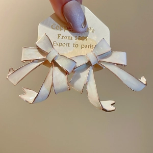Detail of cream white enamel bow earrings with gold metal edges held on a jewelry card