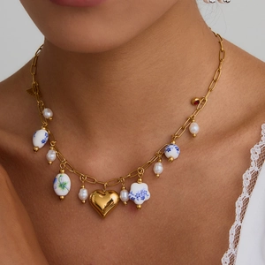 Detail of model wearing a gold chain necklace with blue floral ceramic and pearl beads
