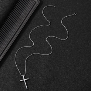 Close-up of a polished stainless steel cross pendant necklace on a black textured background