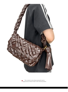 Detail of dark brown woven crossbody bag with oversized tassel knots on a model