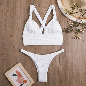 Flat lay of white bikini set with wave texture and wrap top on a dark wood background