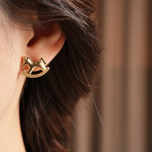 Detailed view of a gold horse stud earring with a textured hammered finish on a model