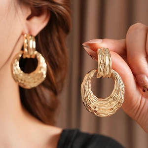 Detailed view of large golden hoop earrings with unique hammered texture and metallic shine