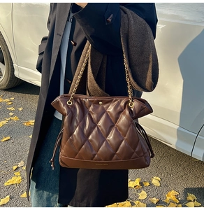 Close-up of brown quilted shoulder bag with gold chain strap in an autumn street setting