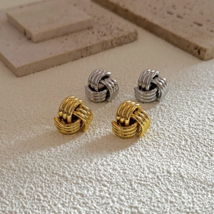 Detail of twisted knot stud earrings in polished gold and silver finish on stone texture
