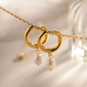 Detail of gold hoop earrings featuring elegant white freshwater pearl pendants