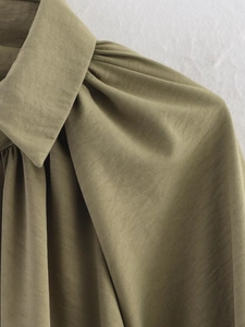 Detail of olive green jacket featuring lapel collar and pleat accents on the shoulder