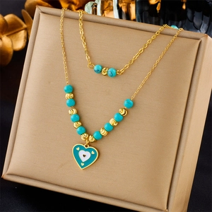Detail of layered gold necklace with turquoise beads and green enamel heart pendant