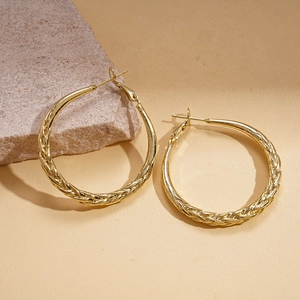 Macro shot of gold hoop earrings with braided texture on rustic stone background