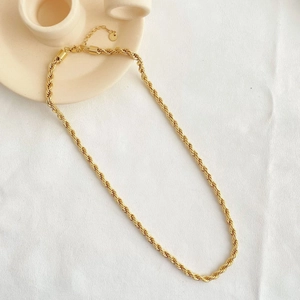 Detailed view of a gold rope chain necklace on a soft white fabric with cream ceramic decor
