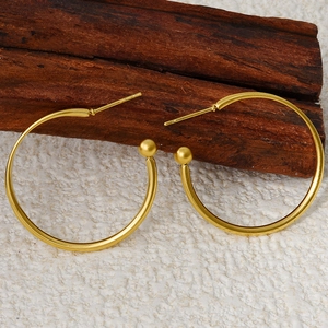 Close-up of minimalist matte gold hoop earrings with small spherical charms on wood
