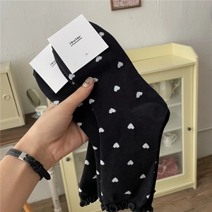 Close-up of black mid-tube socks with white heart patterns and ruffled edges in hand