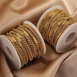 Golden stainless steel ball and bar link chain on white spools over silk fabric