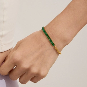 Close-up of gold beaded bracelet with emerald green baguette zircons on a wrist