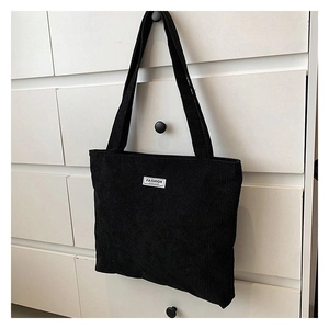 Detail of black corduroy tote bag showing ribbed texture and fashion logo patch