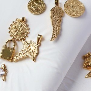 Detailed close-up of 18K gold plated charms including heart, lock and caduceus symbols