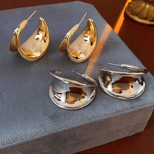 Polished chunky C-shape hoop earrings in gold and silver finish on a grey velvet display