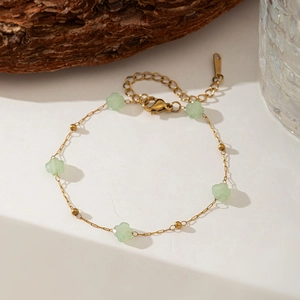 Detailed view of a gold chain bracelet featuring five green floral charms on wood background
