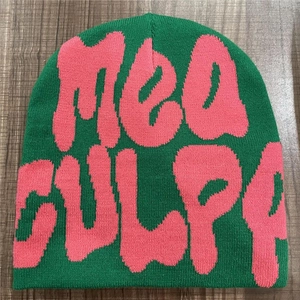 Detailed knit texture of a green and pink MEA CULPA beanie on a dark wood background
