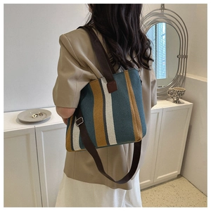 Rear view of striped canvas tote bag in teal and yellow with brown strap on a model