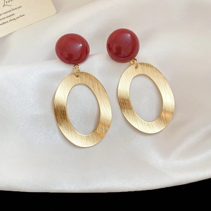 Detailed view of oval brushed metal earrings with glossy red resin beads on silk