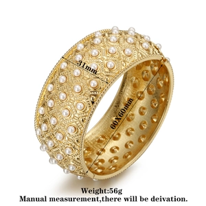 Macro detail of gold textured cuff bracelet featuring white pearls and relief patterns